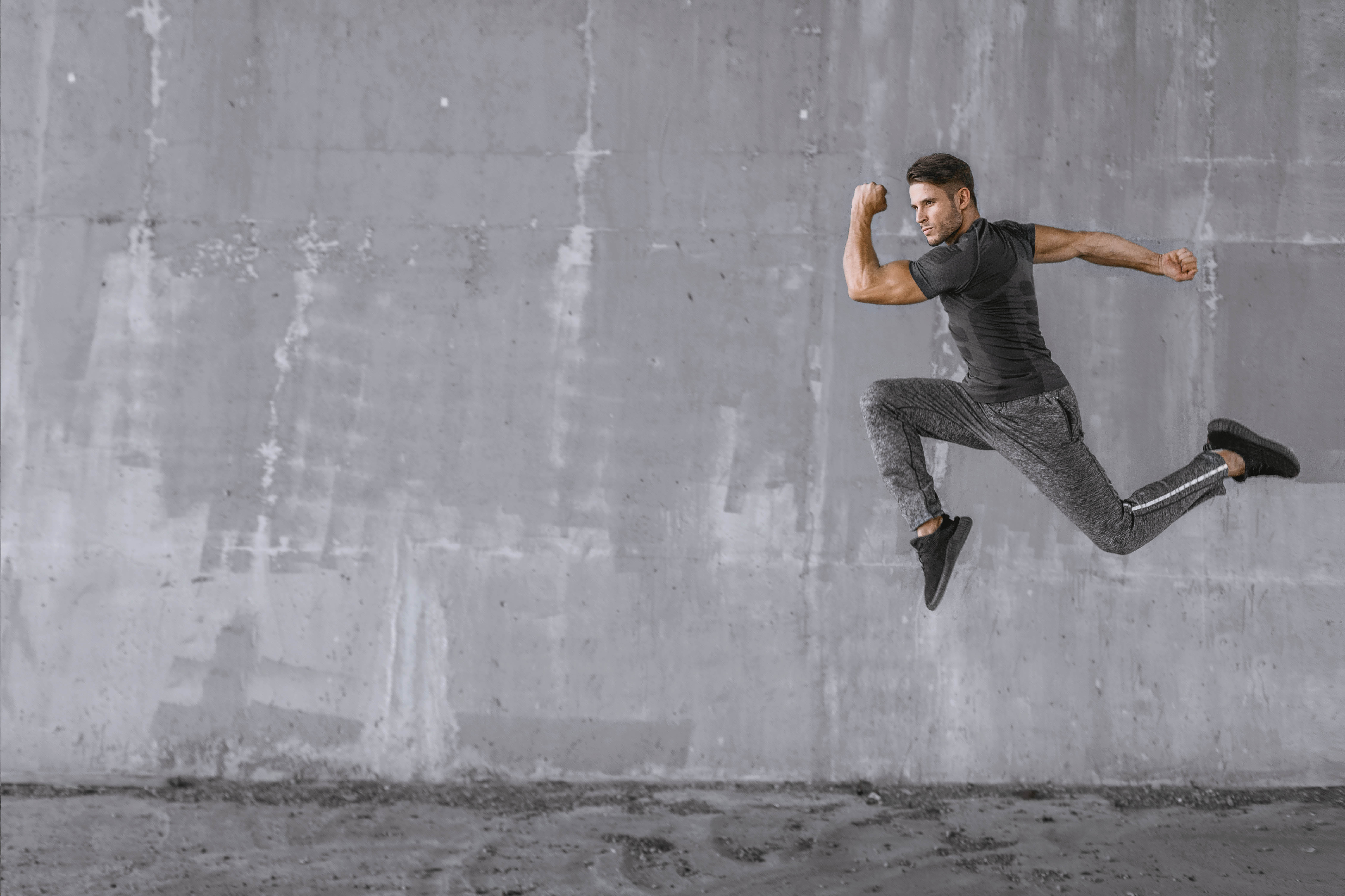 Young fit man doing a running leap in front of a concrete wall
